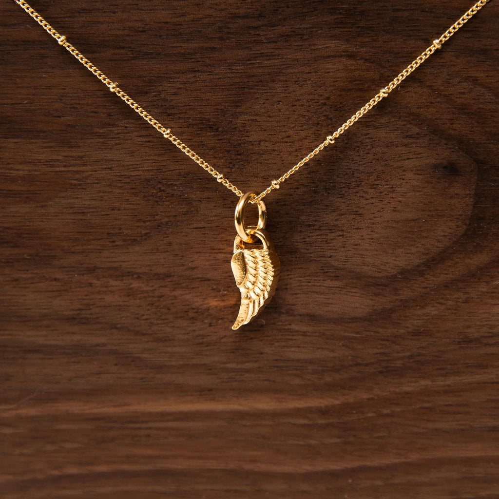 "Gold Wing Necklace" displayed in front of wood background